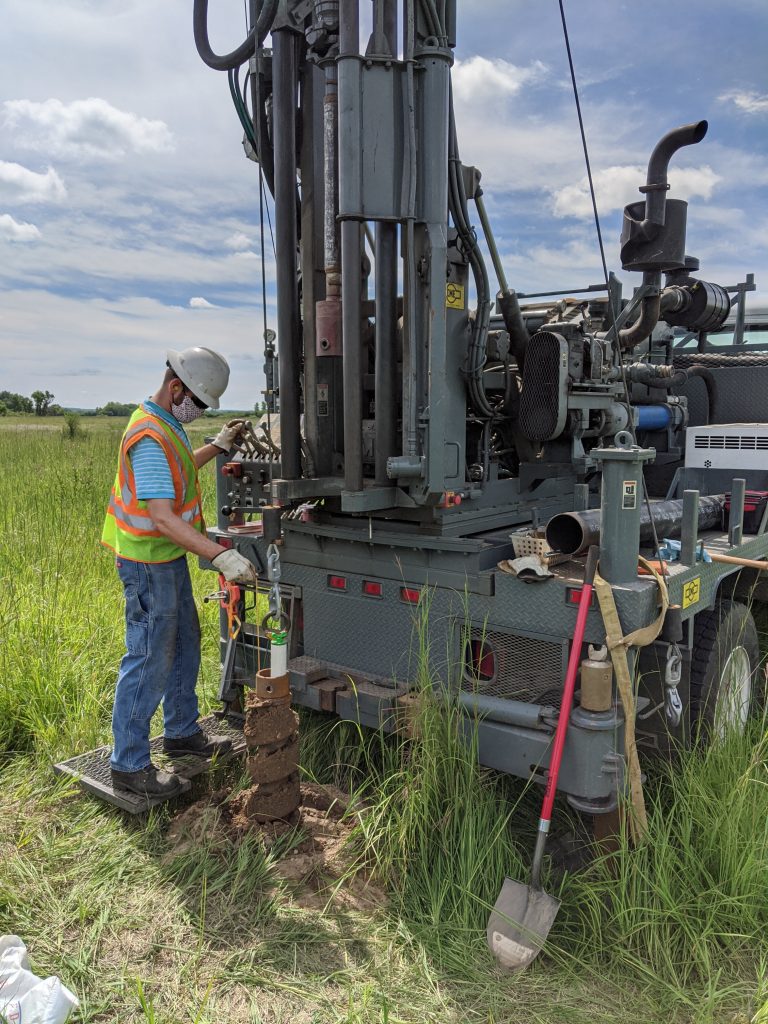 A man operating a well drill, in a field.