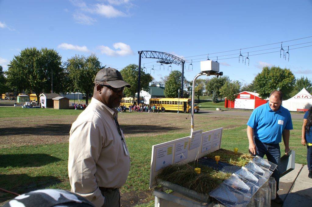 Two men standing next to a display, in a park.