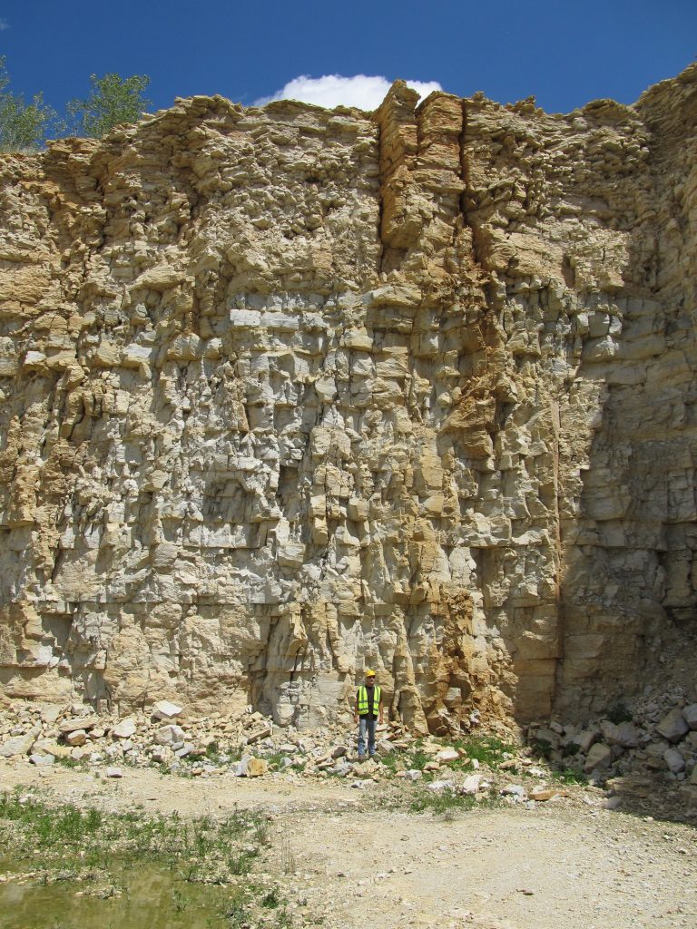 Photograph of Tony Runkel (wearing a neon-colored safety vest) standing in front of an outcrop of fractured rock.