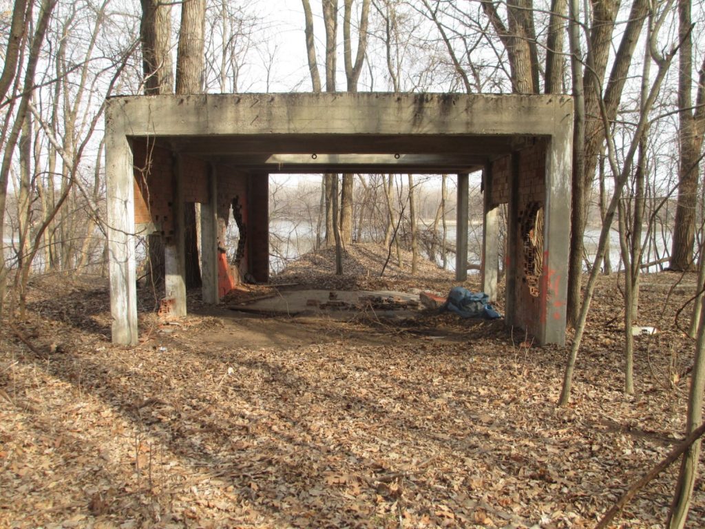 Photo of the Ranney well site. The well is covered with an at-grade concrete lid, located within this dilapidated concrete structure. The Mississippi River is in the background.